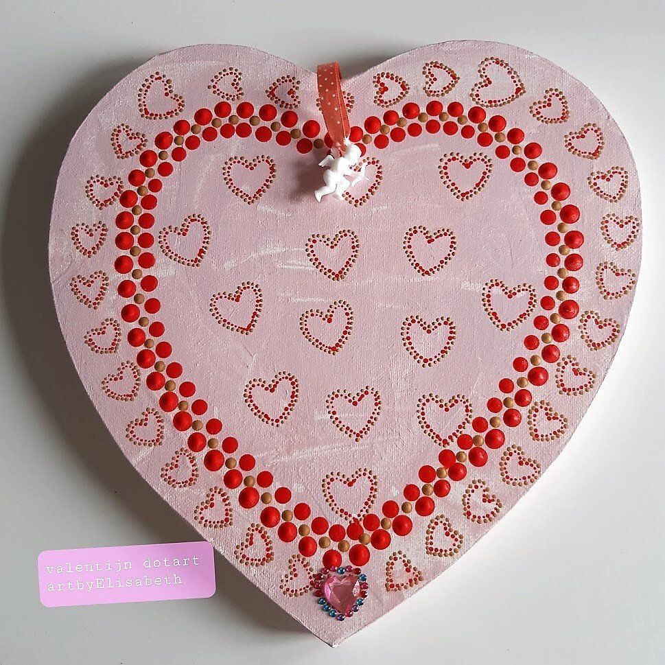 Roze hartvormige decoratie met rode kralenrand en kleine hartjes. Een Cupido en een met juwelen versierde hanger hangen eraan.