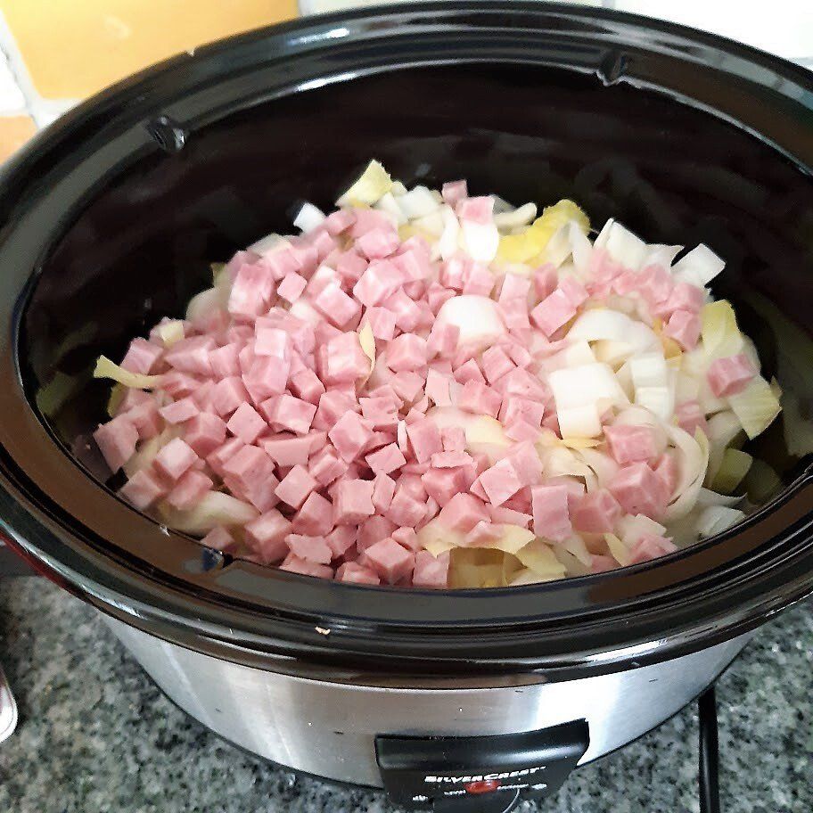 Ham en uien in blokjes gesneden in een zwarte slowcooker, klaar om te koken.
