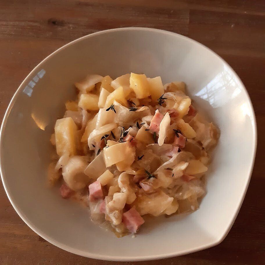 Een kom aardappel- en hamstoofpot met kruiden.