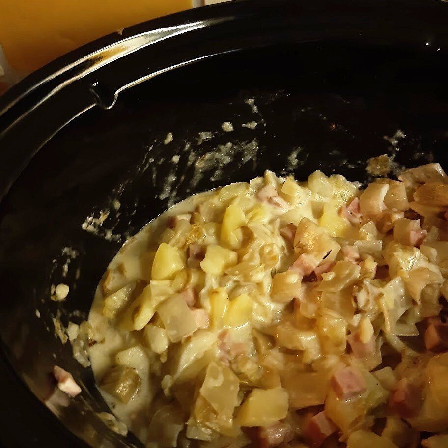 Romig gerecht met blokjes aardappel, ham en ui, bereid in een zwarte slowcooker.