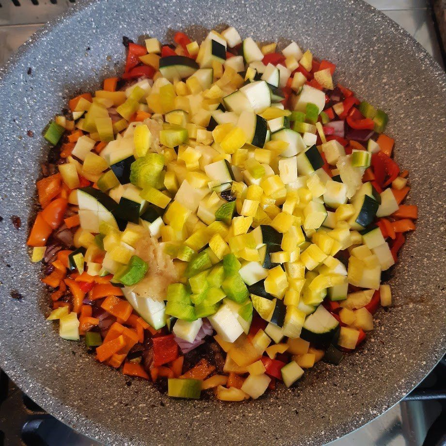 Groenten (courgette, paprika, ui, wortel) worden in stukjes gesneden en in een pan gebakken.