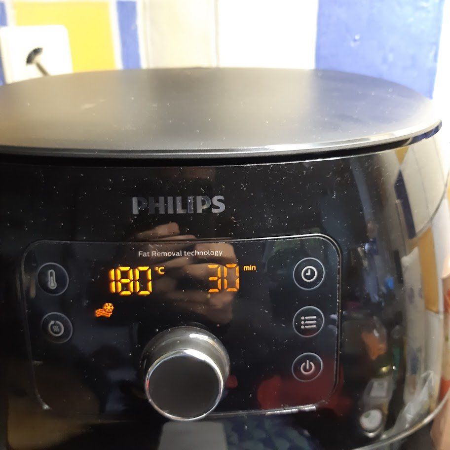 Een zwarte Philips airfryer met digitaal display waarop 180°C en 30 minuten worden weergegeven, knoppen en een draaiknop.