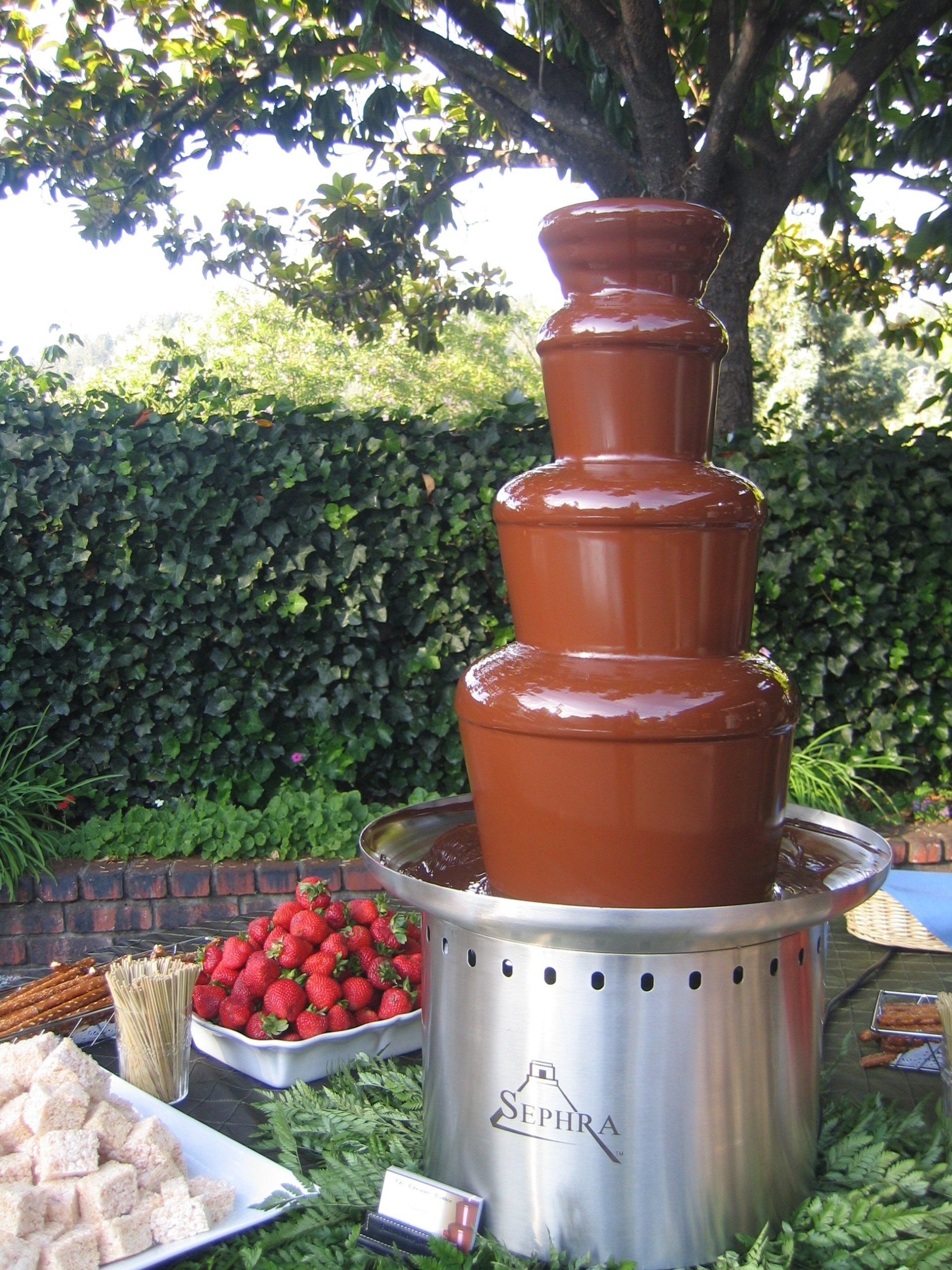 A chocolate fountain with strawberries in the background