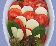 Eine weiße Schüssel gefüllt mit Tomaten, Mozzarella, Basilikum und Salat.