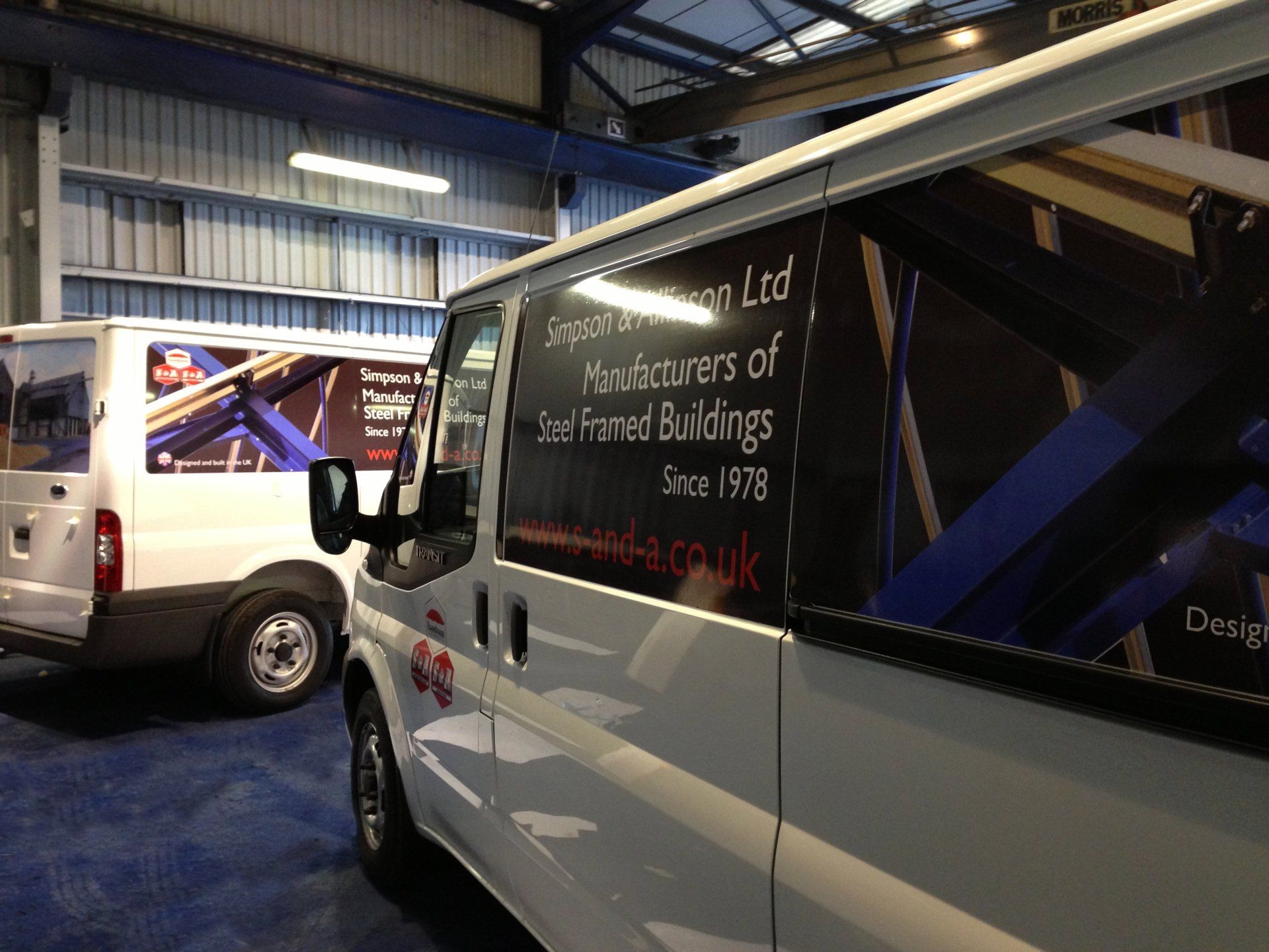 A white van is parked in a warehouse with other vans.