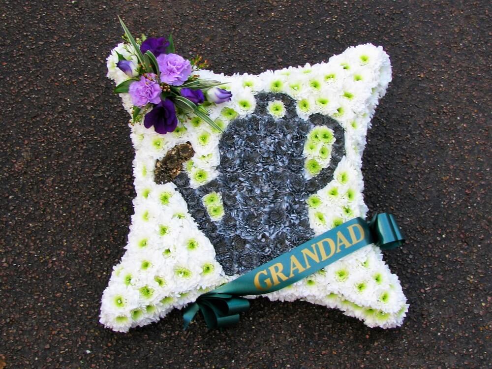 11. 18” white Cushion with custom made silver Watering Can to the centre, ribbon sash and purple posy