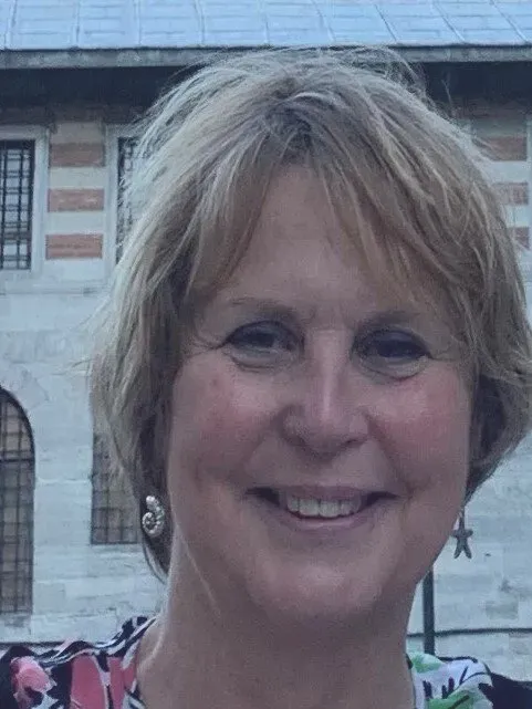 Woman with short blond hair smiles, set outdoors in front of a stone building.