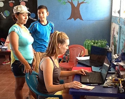 Woman using a laptop, two people watch in a colorful classroom.