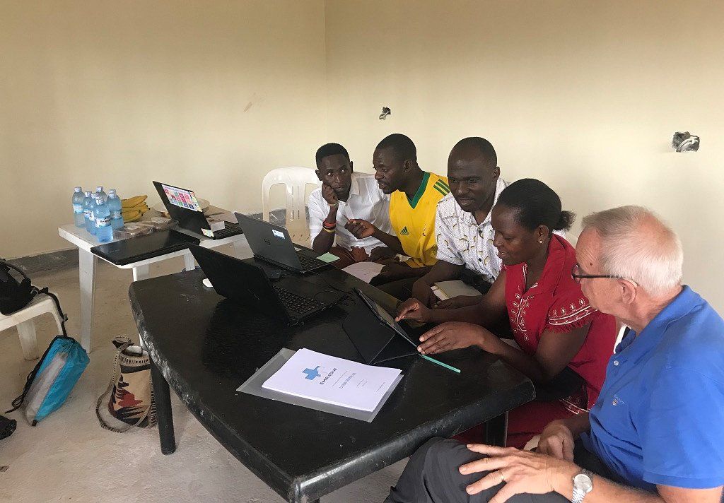 Group of people using laptops at a table, possibly a training session. Indoors, light-colored walls.
