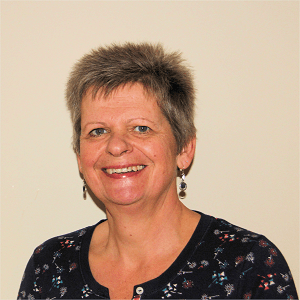 Smiling woman with short gray hair, wearing dark blue floral shirt, earrings.