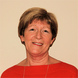 Woman with short brown hair smiles, wearing a red sweater, against a beige wall.