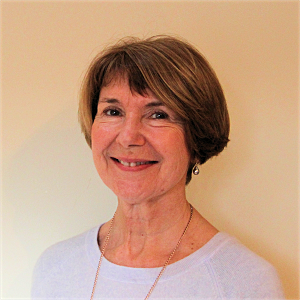 Woman with short brown hair smiling, wearing a white sweater and gold necklace.