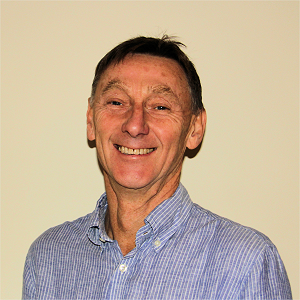 Smiling older man in a blue striped shirt against a plain background.