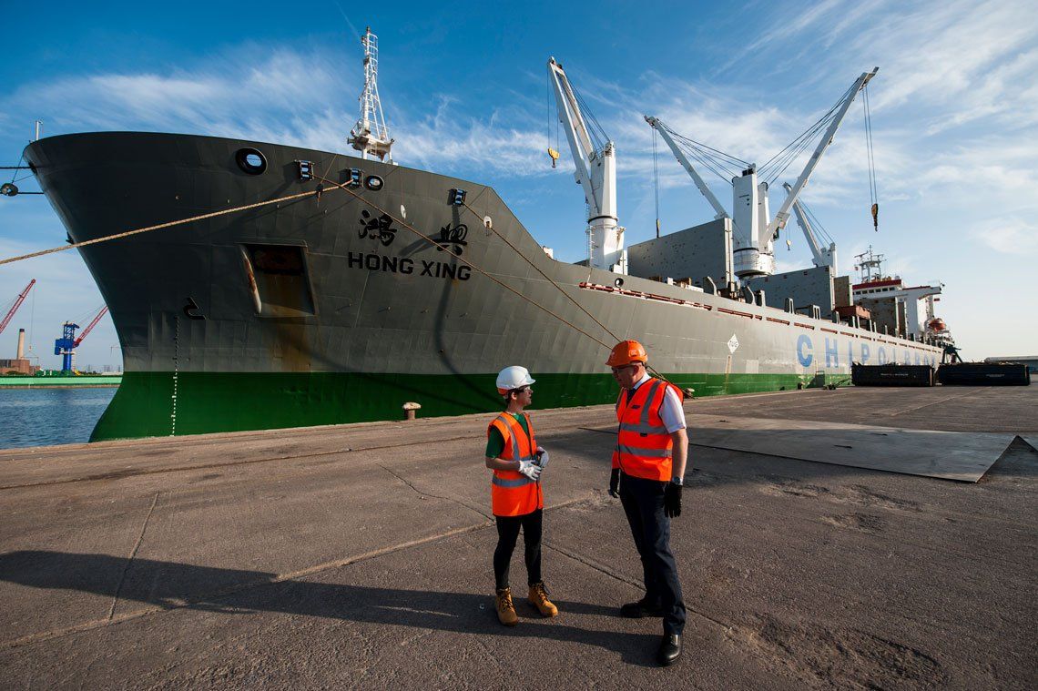 Two men standing in front of a large ship that says hong kong