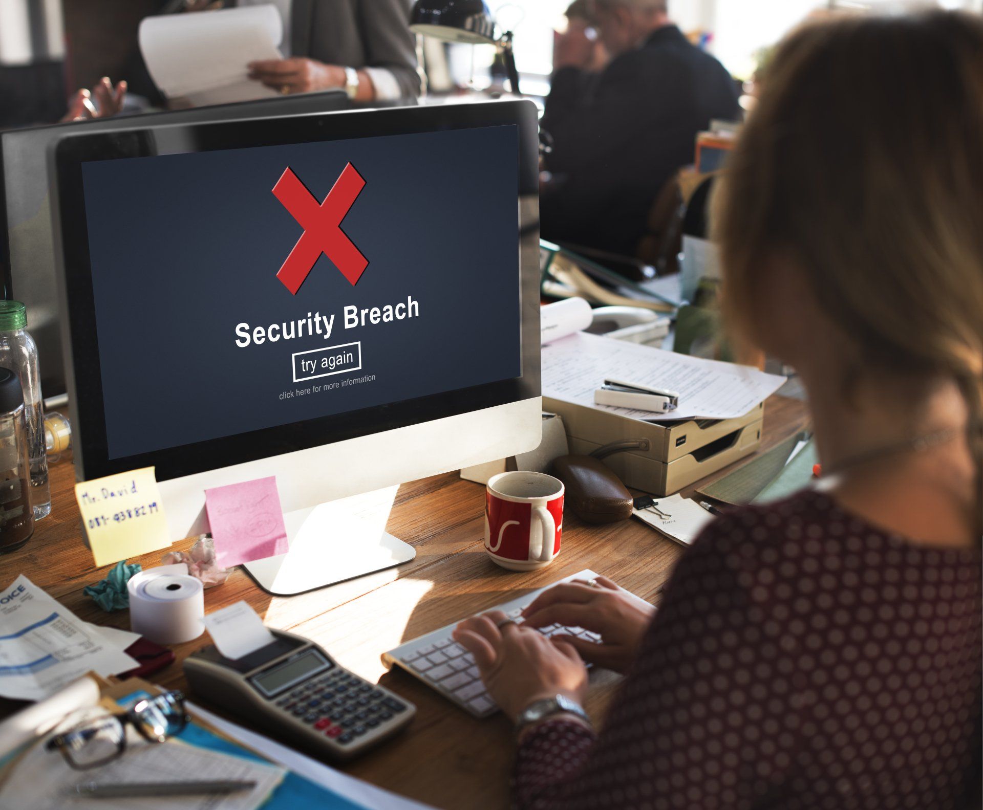A woman sits at a desk with a computer that says security breach