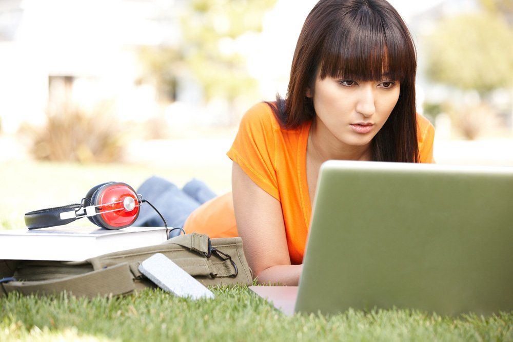 A woman is laying on the grass using a laptop