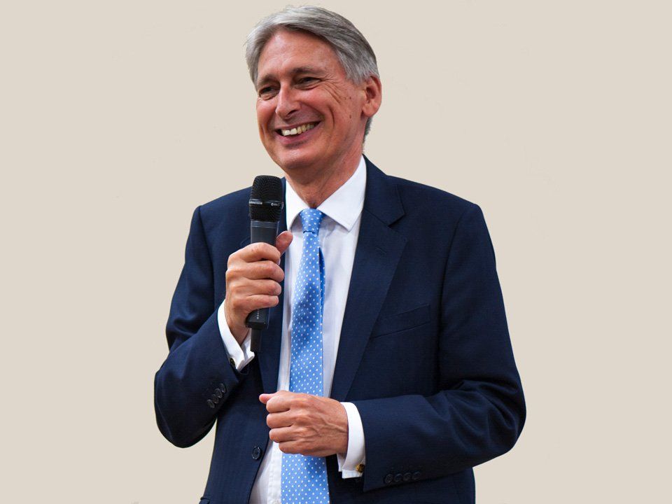 Philip Hammond in a suit and tie is holding a microphone and smiling