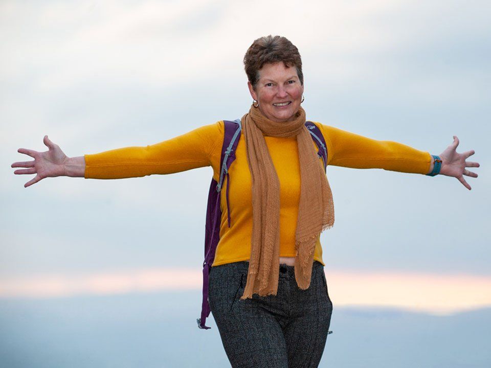 A woman in a yellow sweater and scarf is standing with her arms outstretched