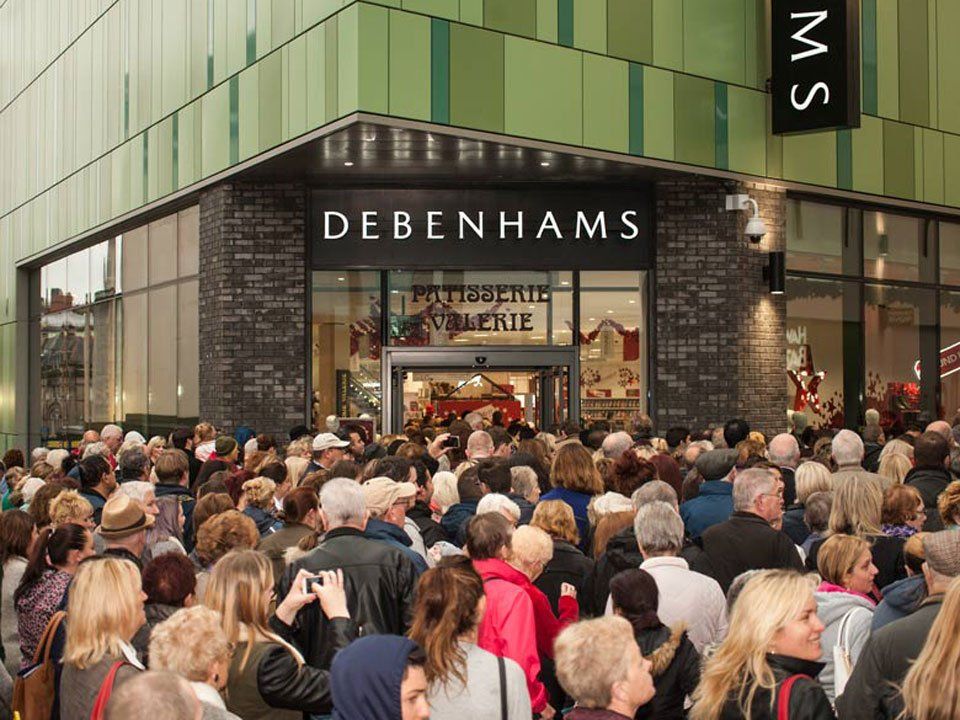 A crowd of people are gathered outside of a debenhams store