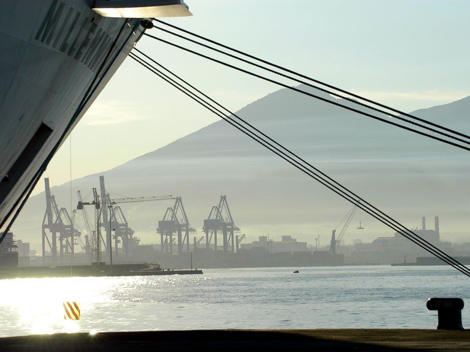 A large ship is docked in Naples harbour with mountains in the background