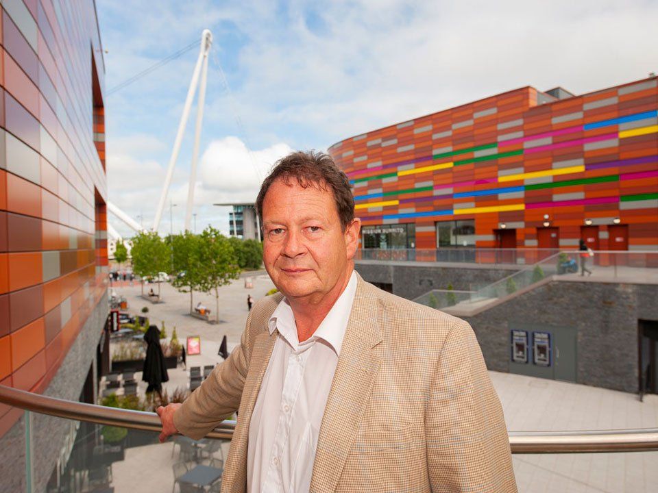Matthew Evans MBE in a suit stands in front of a colorful building