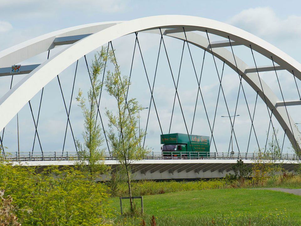 A green truck is driving under an arched bridge