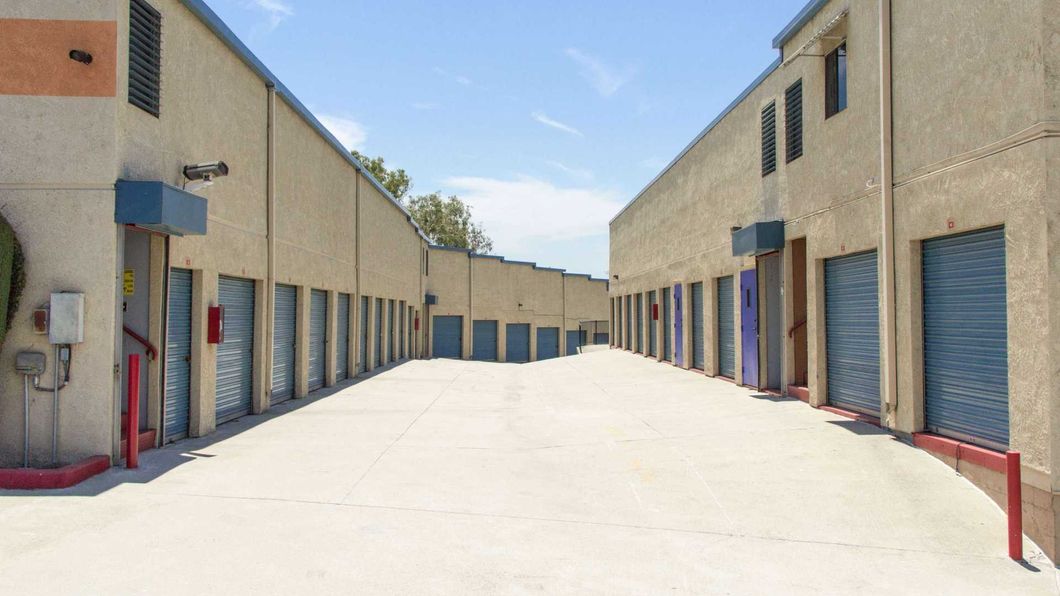 Empty industrial alley with beige buildings, blue roll-up doors, and red railings under a bright sky