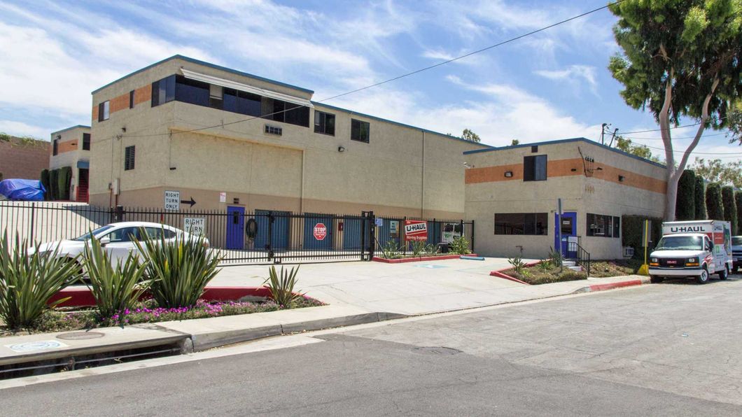 Two-story beige building with parked cars, a sidewalk, and desert landscaping under a blue sky