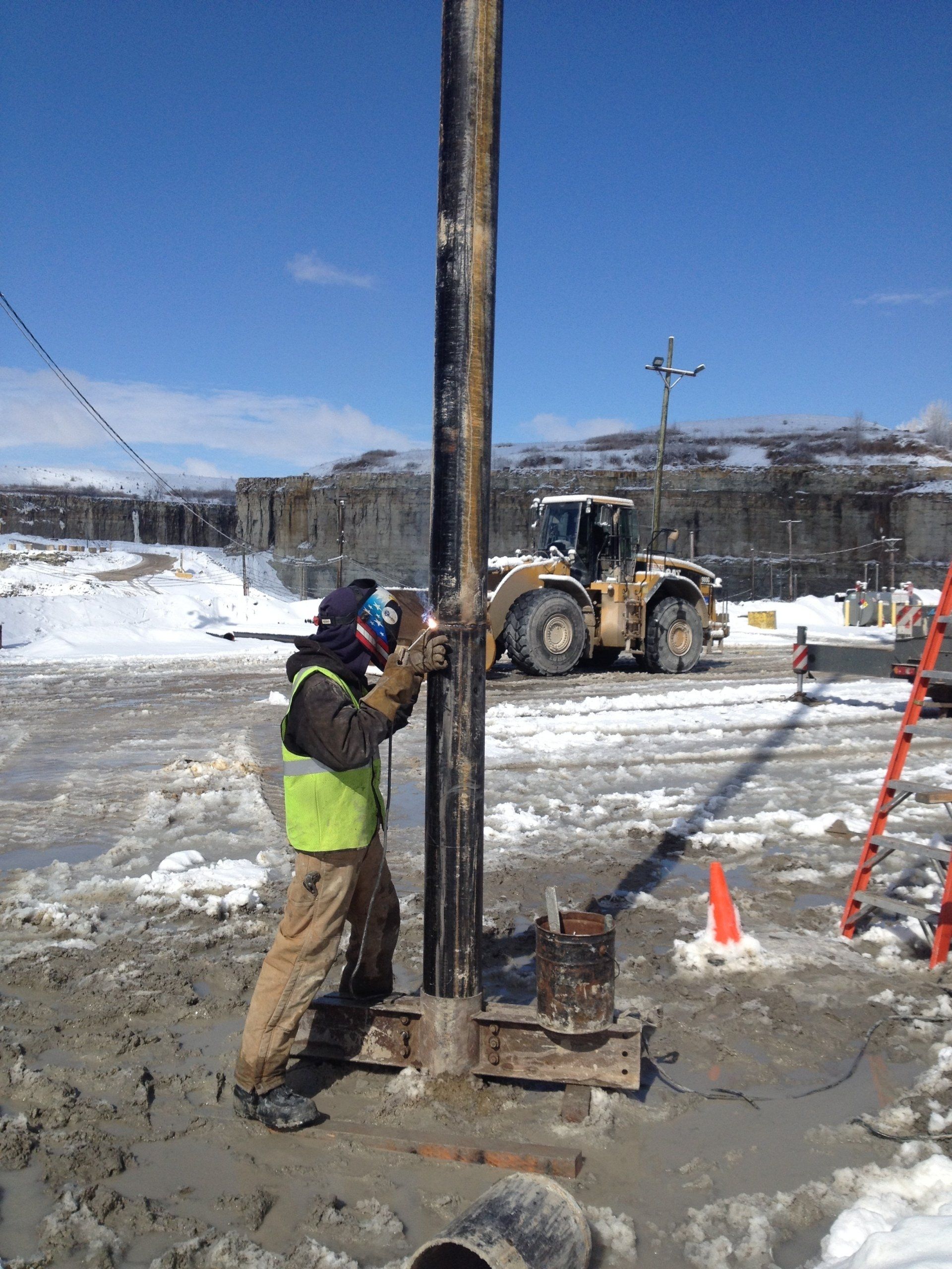 a man is working on a pole in the snow with a bulldozer in the background.