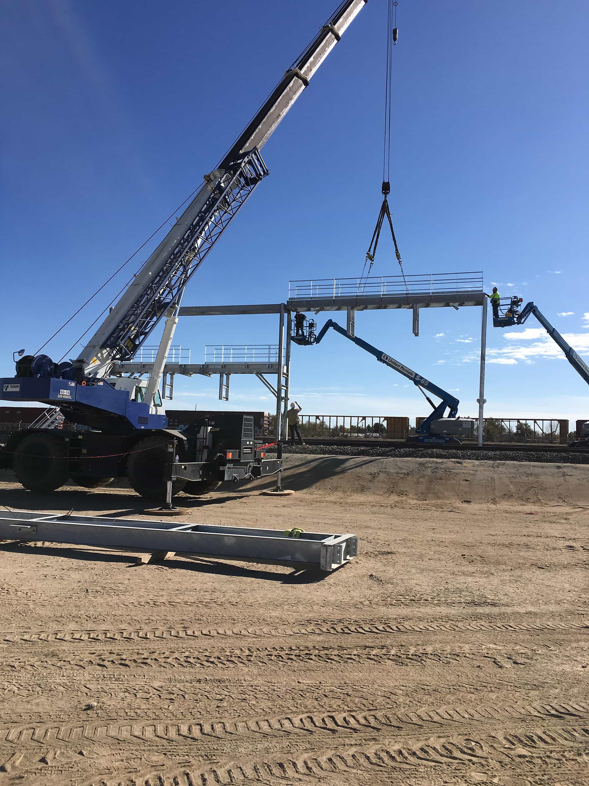 a crane is lifting a metal structure in a dirt field.