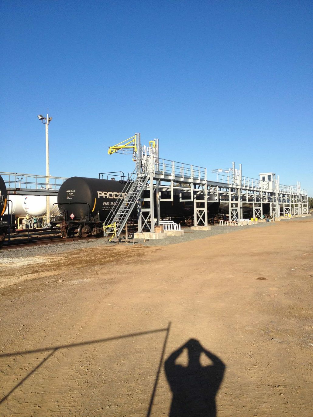 a shadow of a person is cast on the ground in front of a train yard.