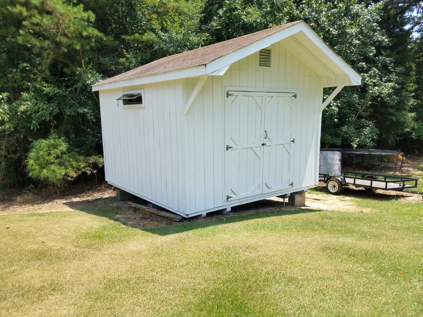 a white shed is sitting on top of a lush green field .