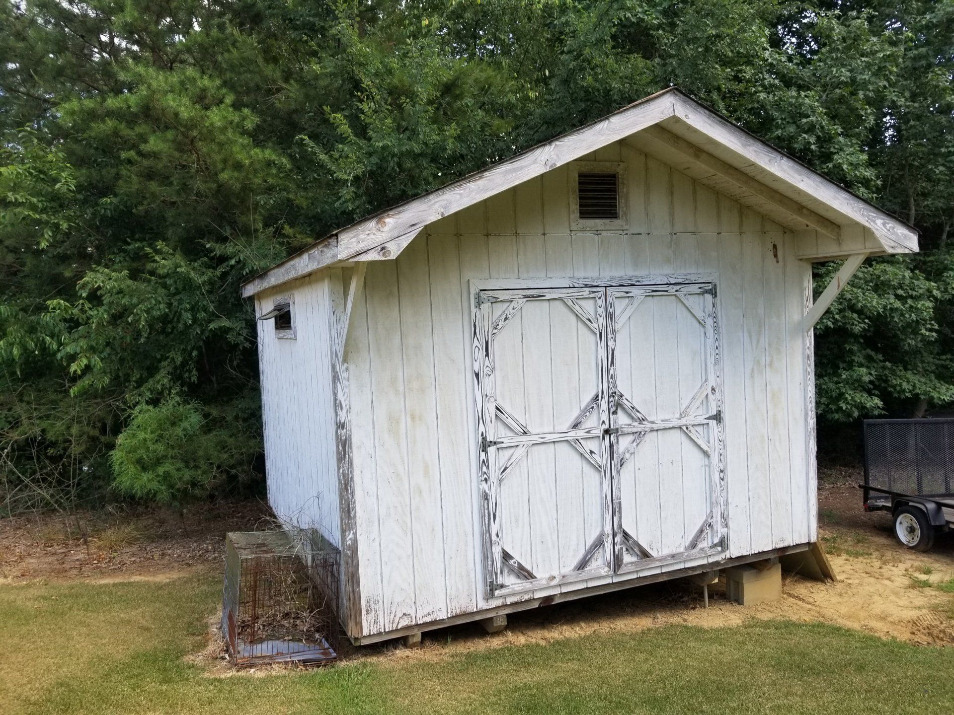 a white shed is sitting in the middle of a grassy field .