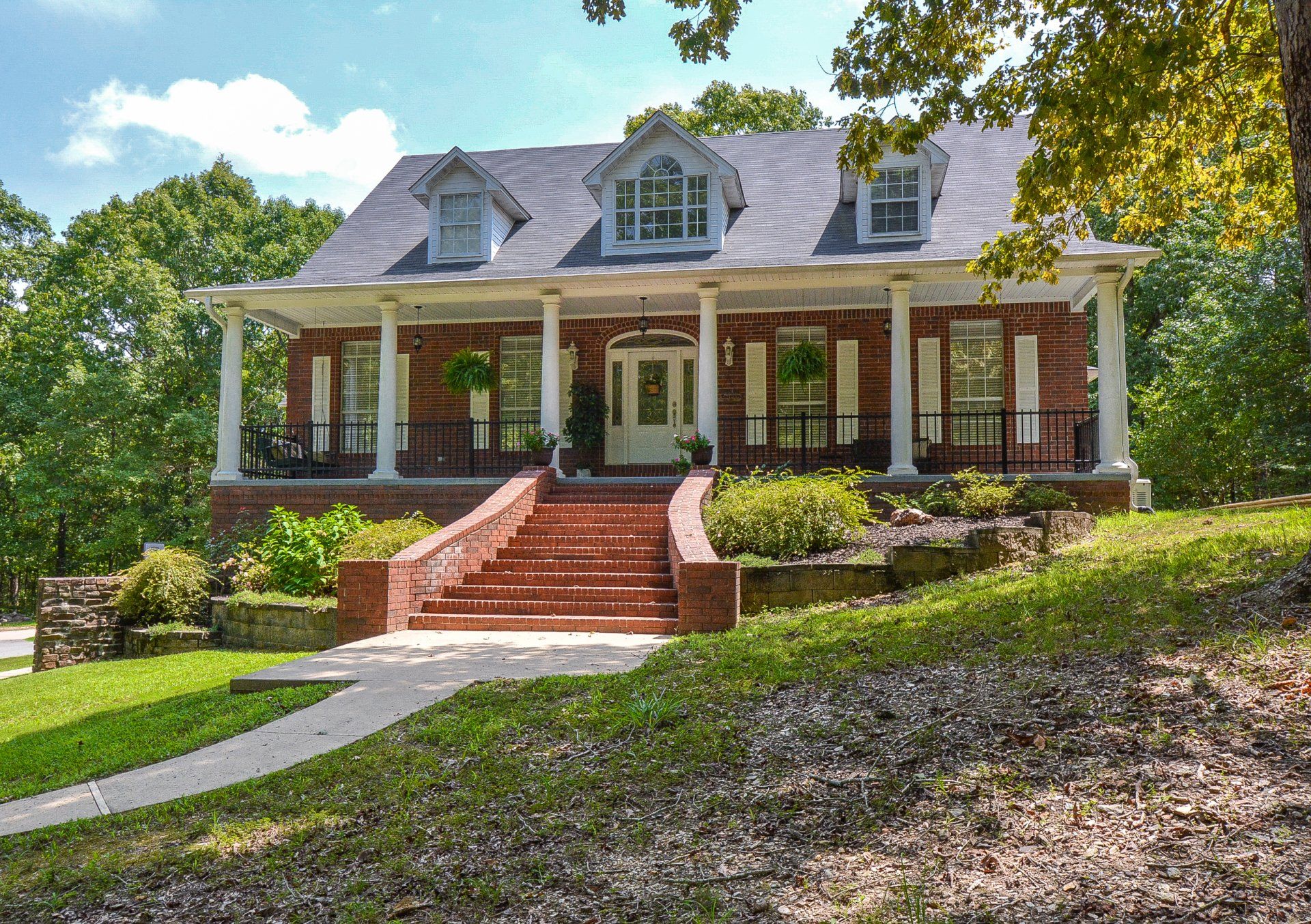 Red brick home with white columns, front steps, and a green lawn.