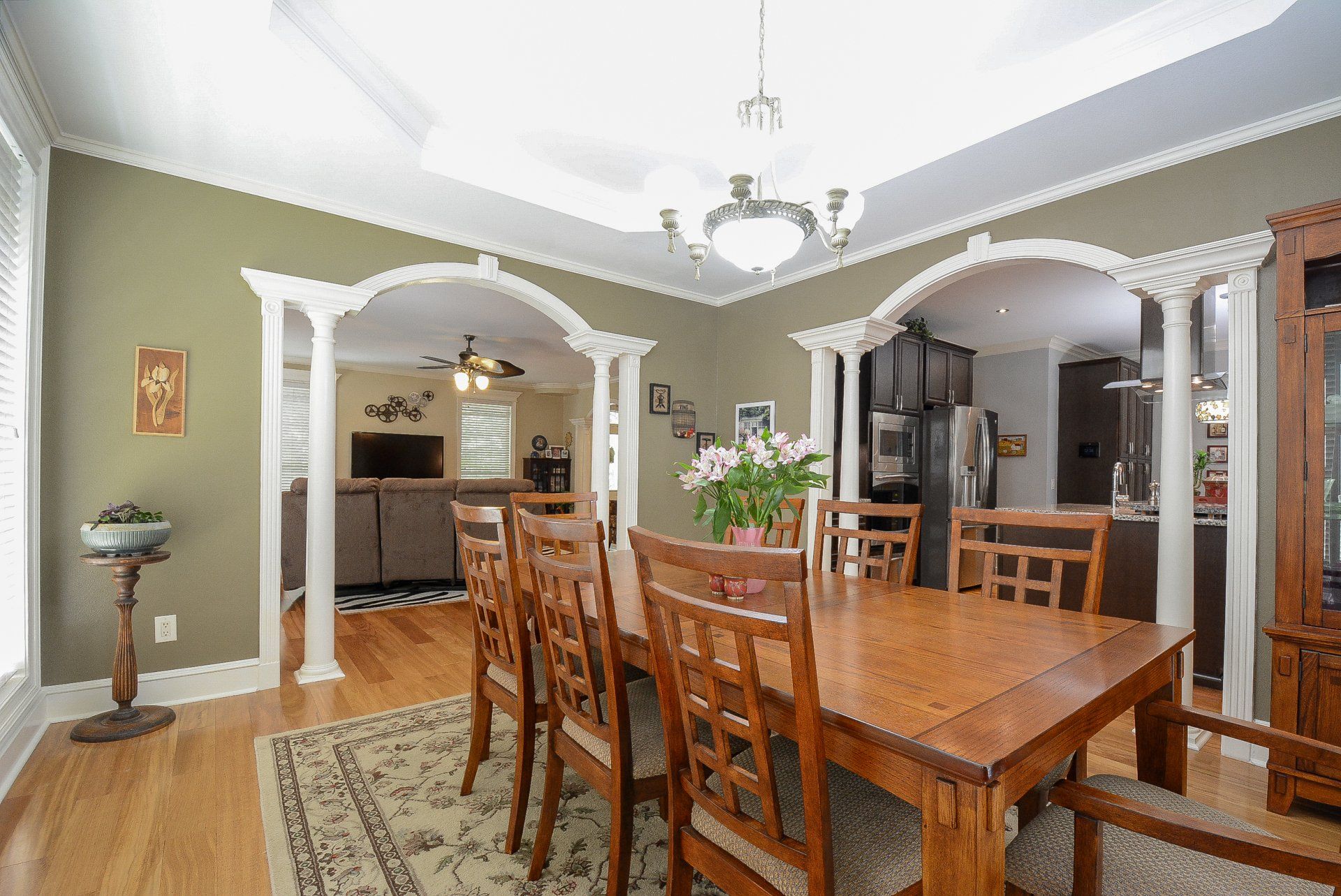 Dining room with wooden table, chairs, archways, and view to living room.