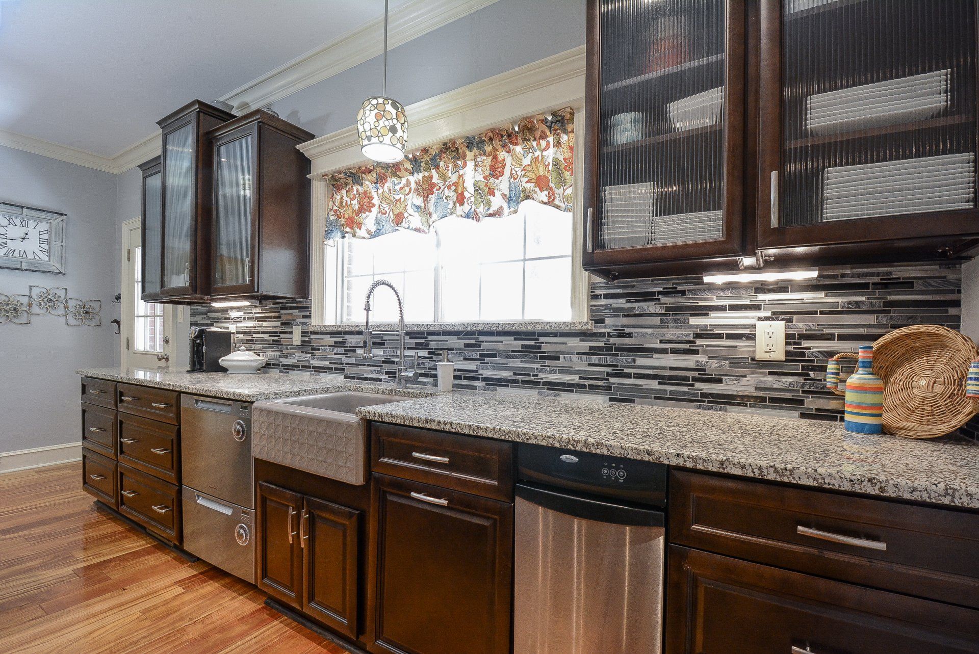 Kitchen with dark cabinets, granite countertops, stainless steel appliances, and a window with patterned curtains.