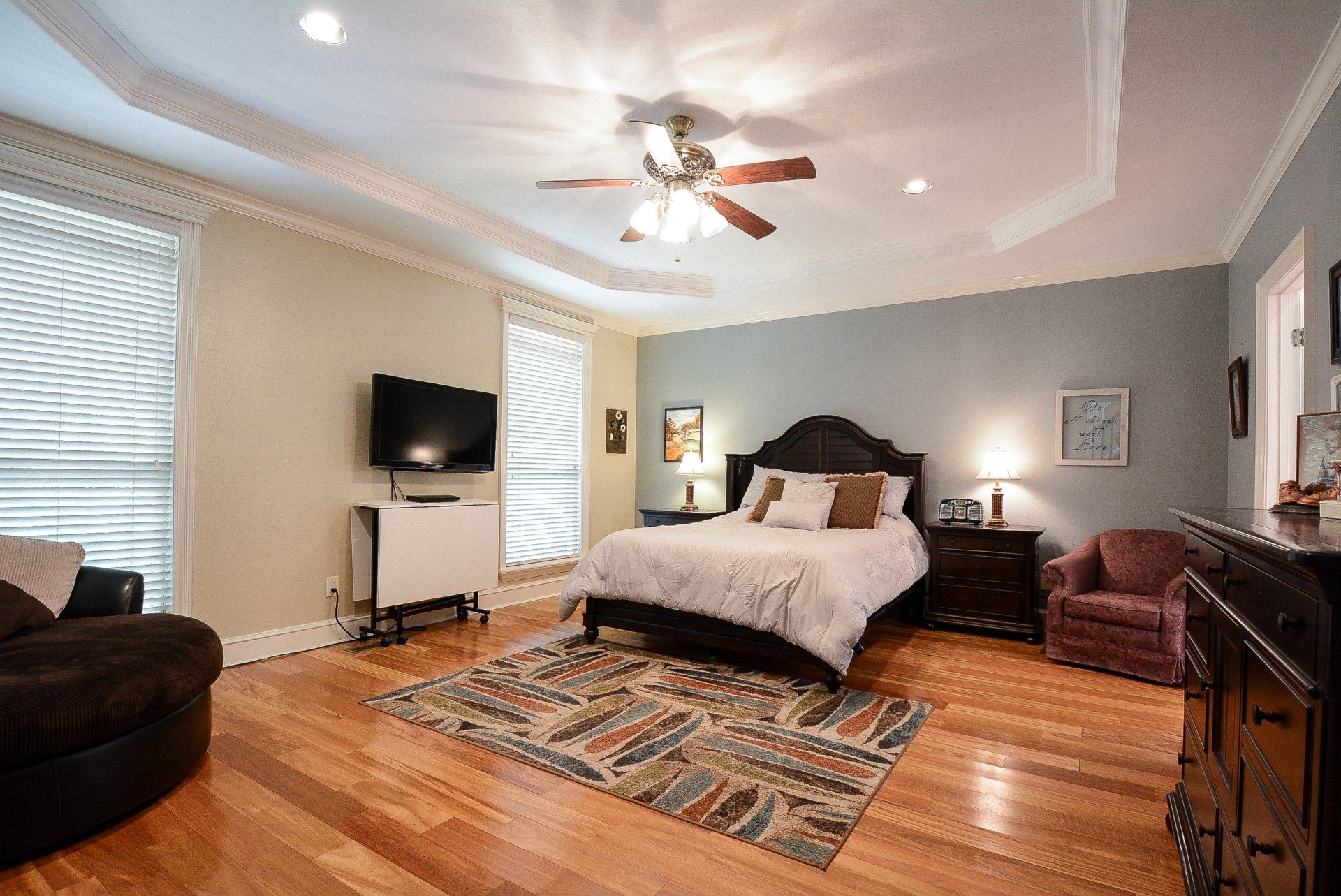 Bedroom with hardwood floors, queen bed, TV, and a ceiling fan. Blue, beige, and brown colors.
