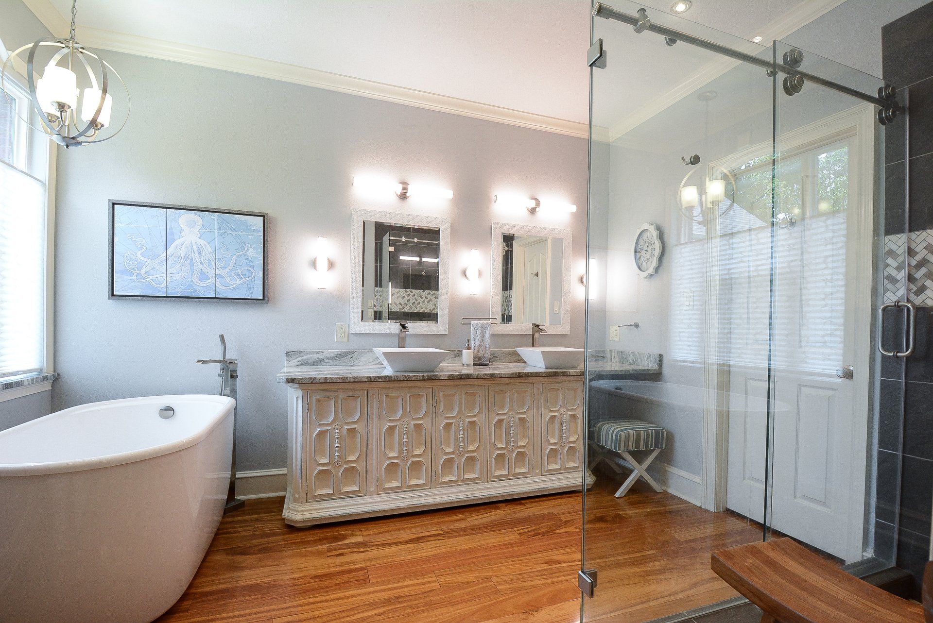 Luxurious bathroom with double vanity, freestanding tub, glass shower, and TV. Light wood floor and light blue walls.
