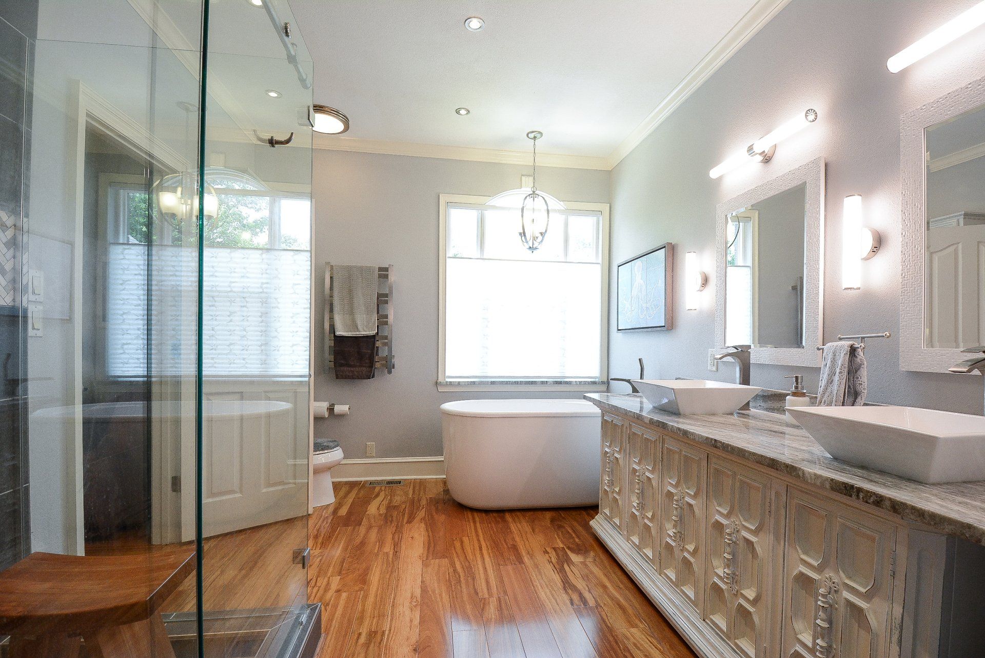 Luxurious bathroom with white fixtures, wood floors, and a glass-walled shower.