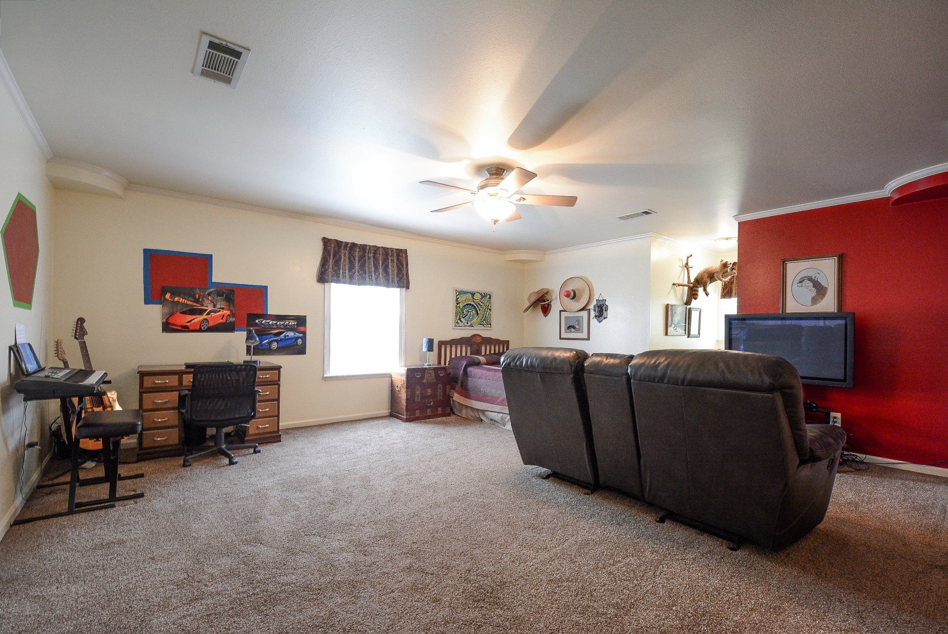 Living room with recliner sofa, desk, and TV on a red wall, with tan carpeting.