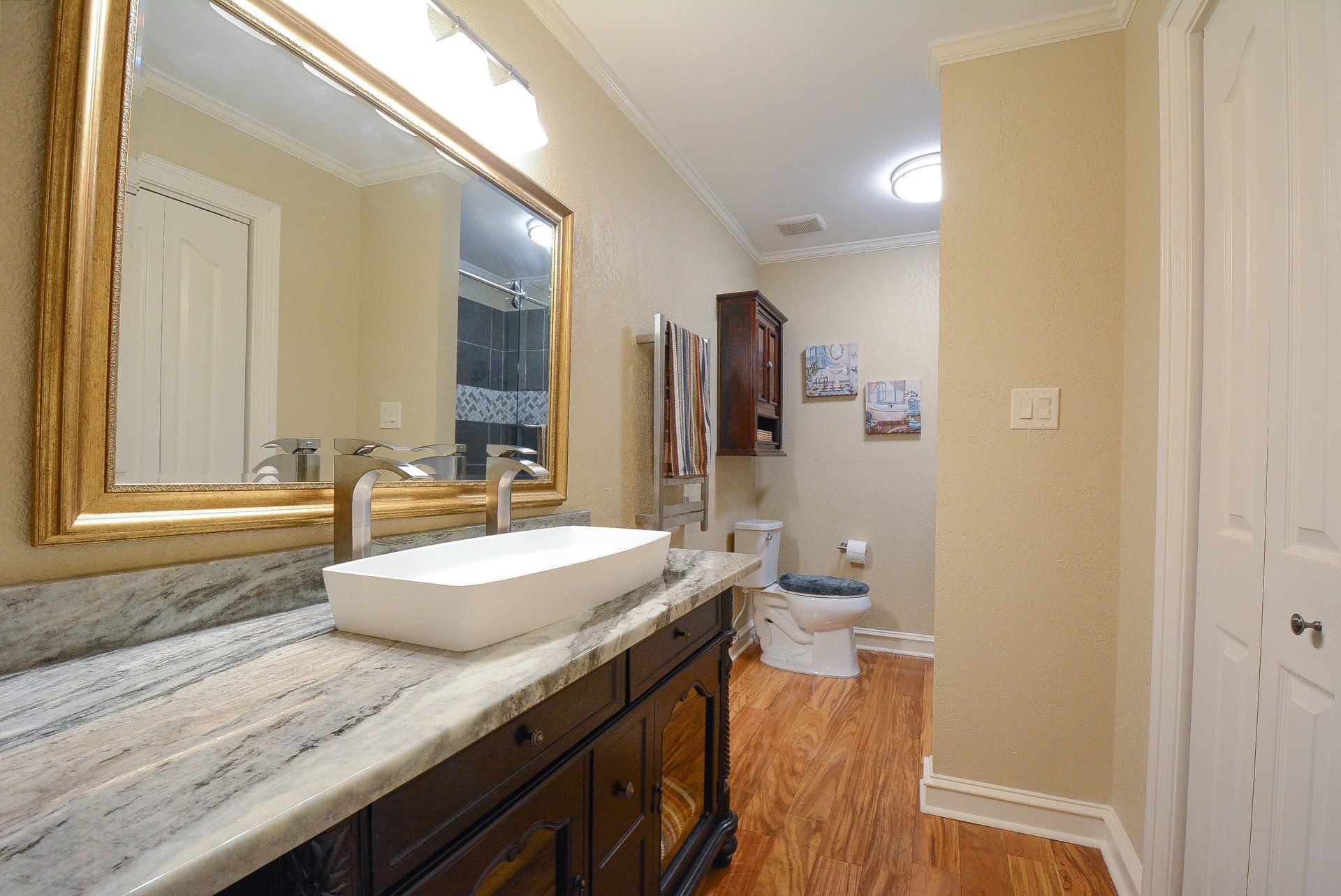 Bathroom with marble countertop, white sink, large mirror, and wood-look flooring.