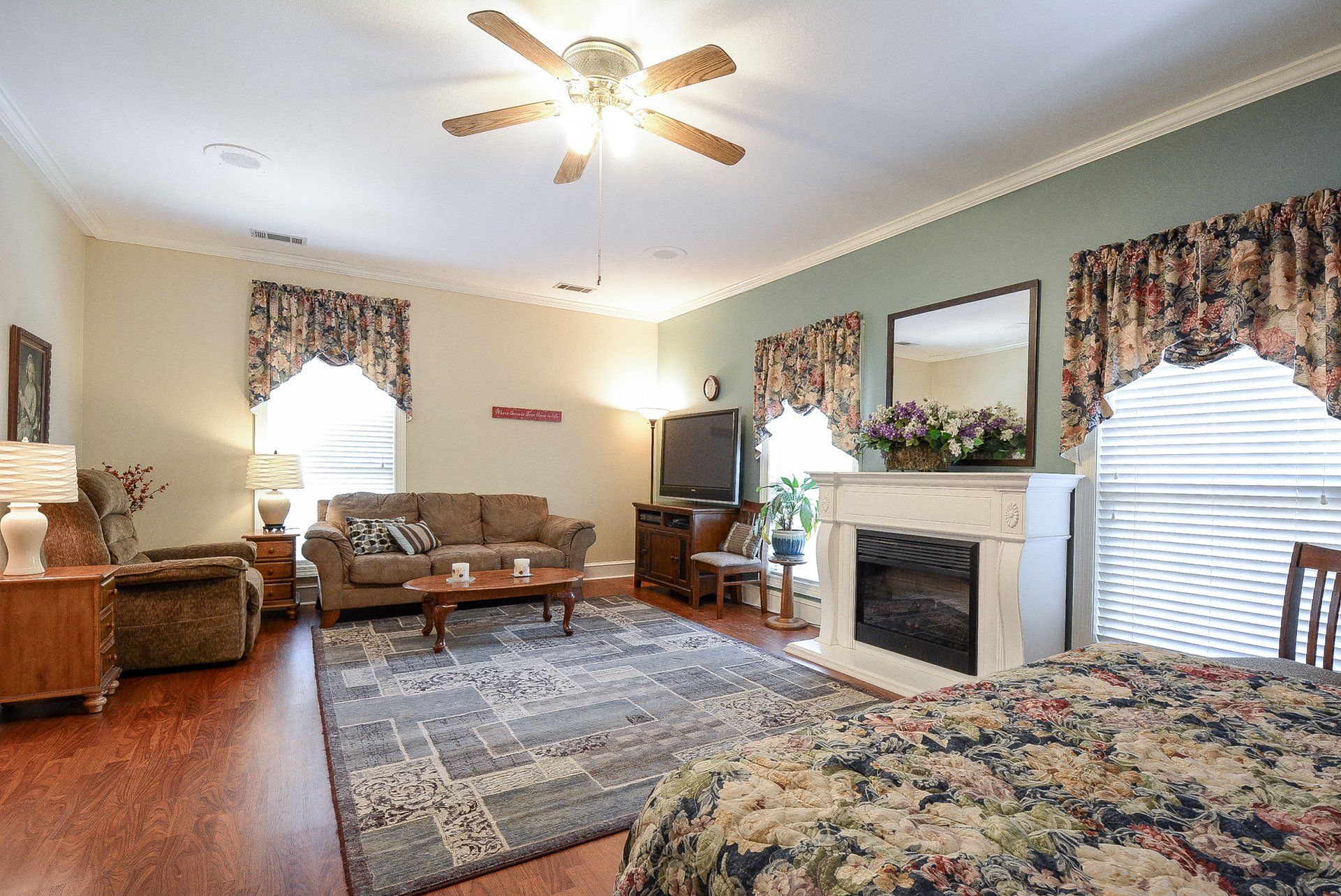 Spacious living area with brown sofa, fireplace, rug, and floral curtains.