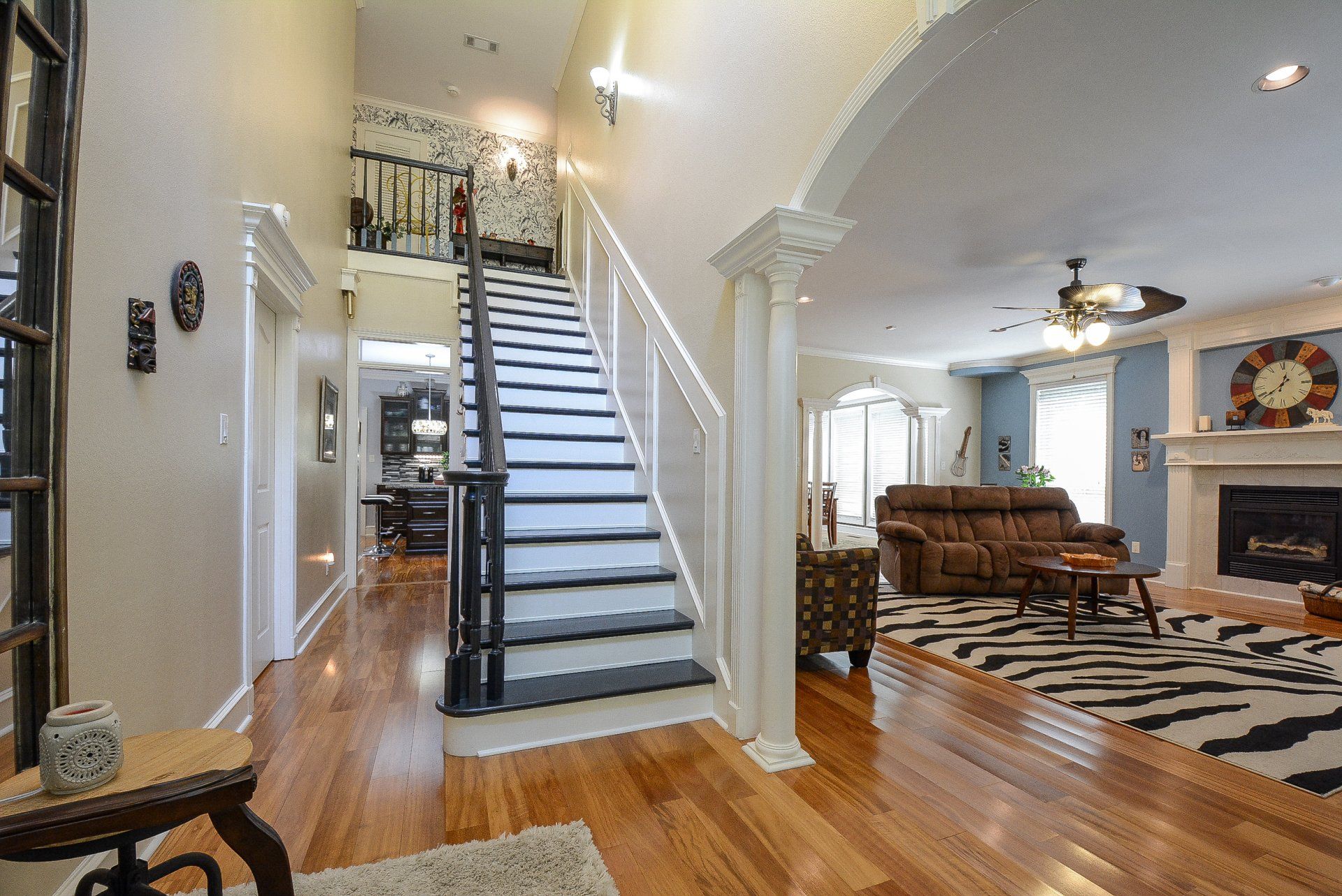 Wooden floor foyer with staircase leading up, open to a living room with zebra rug and fireplace.