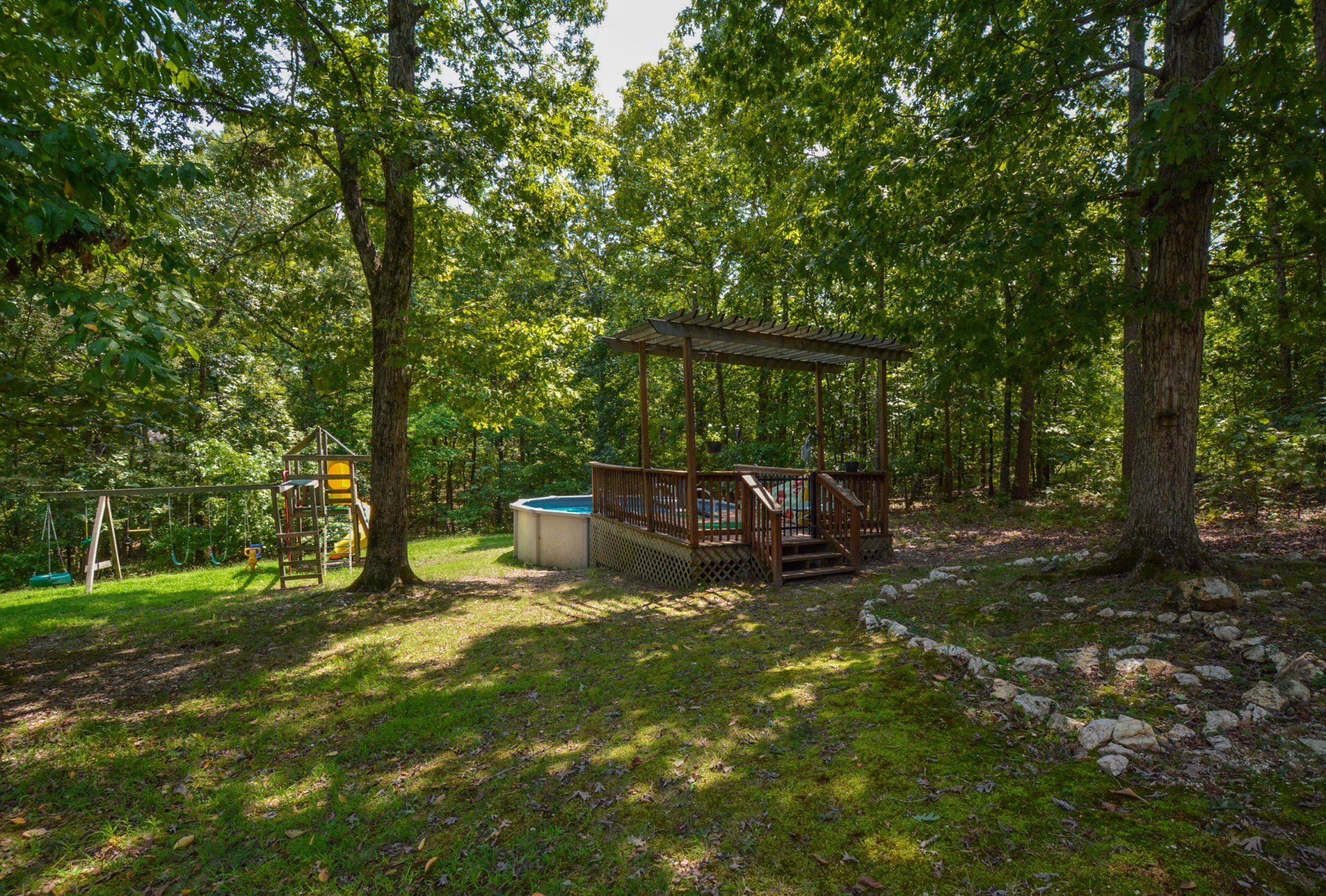 Wooden deck with a hot tub under a pergola, set in a wooded area.