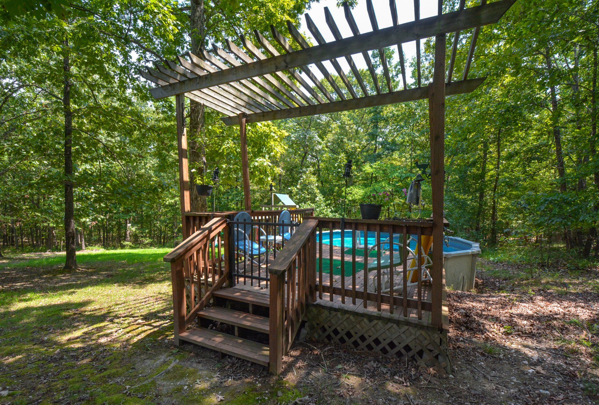 Wooden deck with hot tub, under a pergola, in a wooded area.