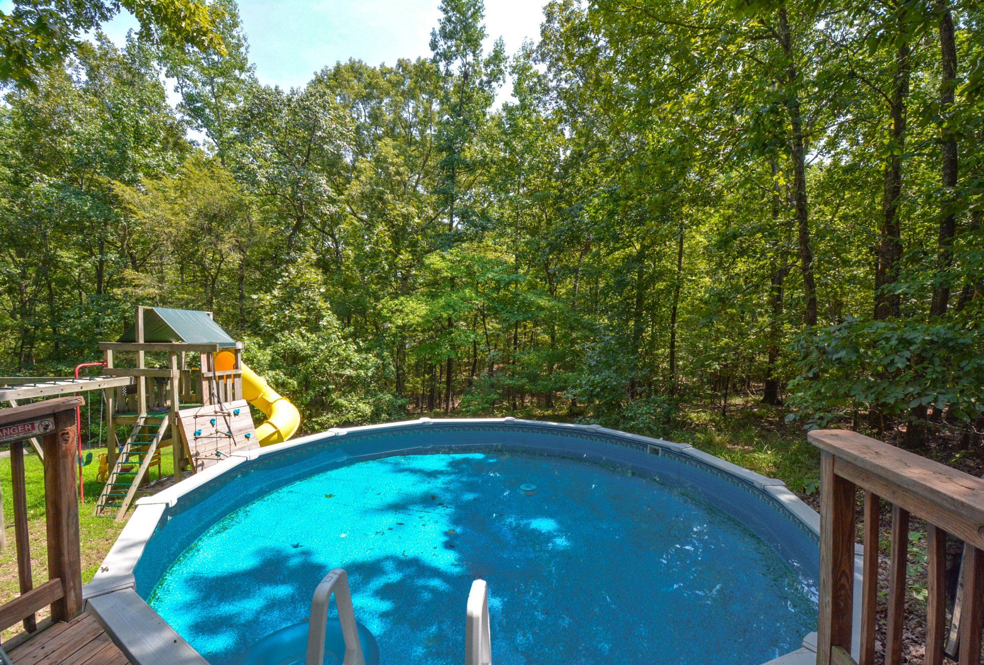 Round pool in wooded backyard with play structure.