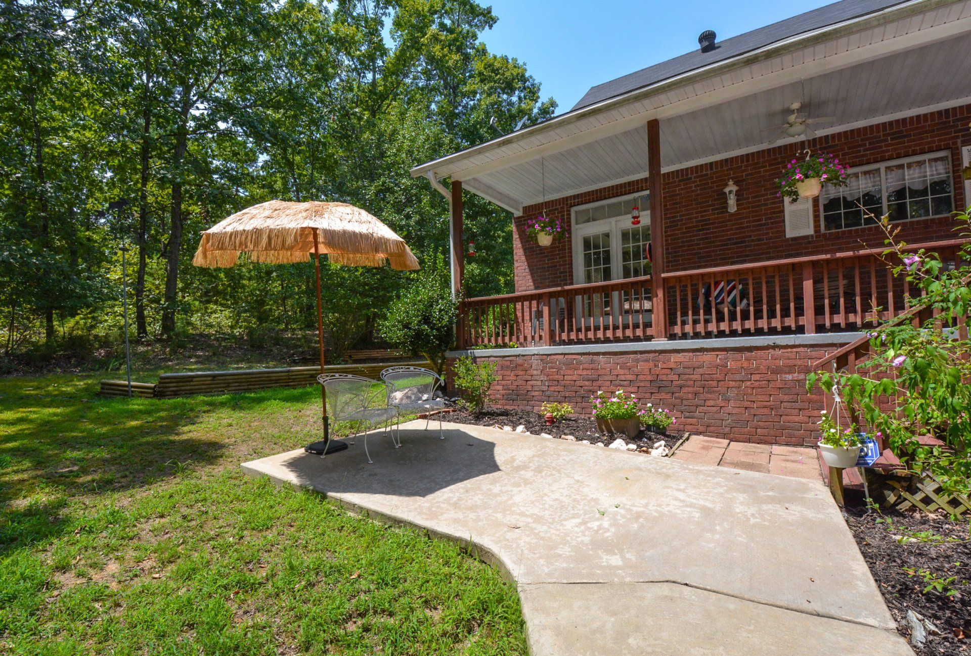 Brick house with porch, trees, and an umbrella over a patio.