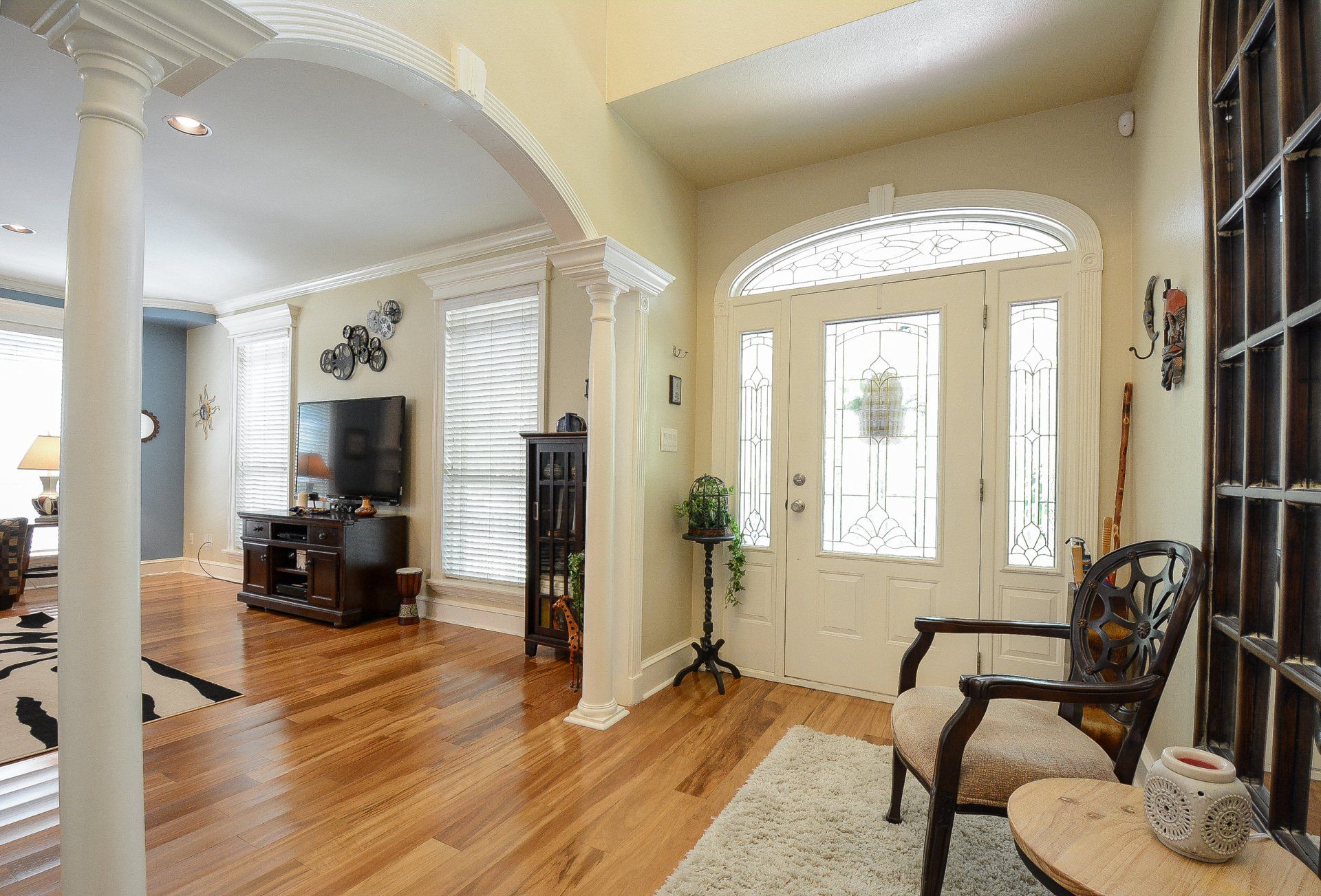 A bright entryway with a white door, hardwood floors, and columns. A chair sits on a rug.