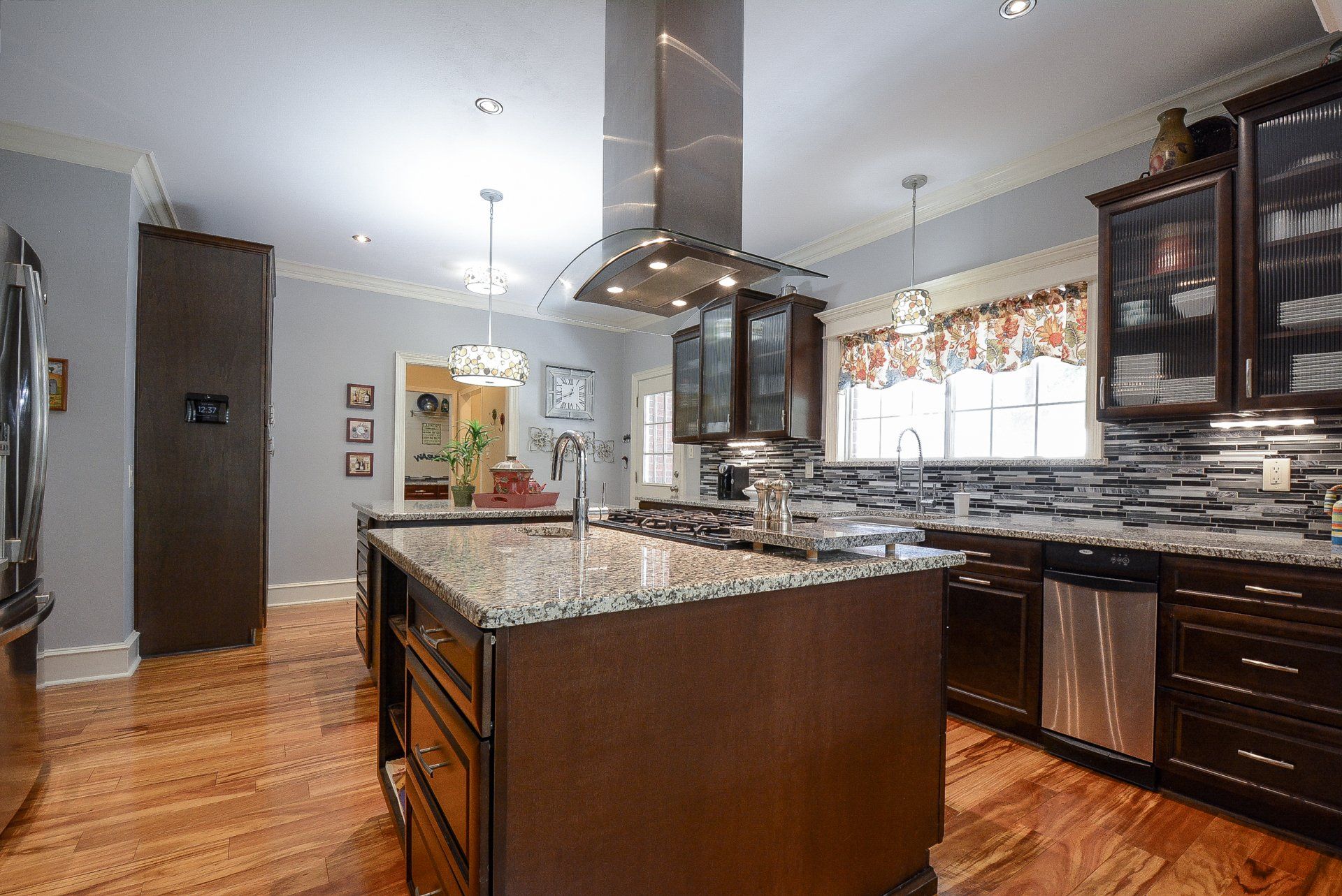 Spacious kitchen with a brown island, stainless steel vent hood, and dark cabinets.