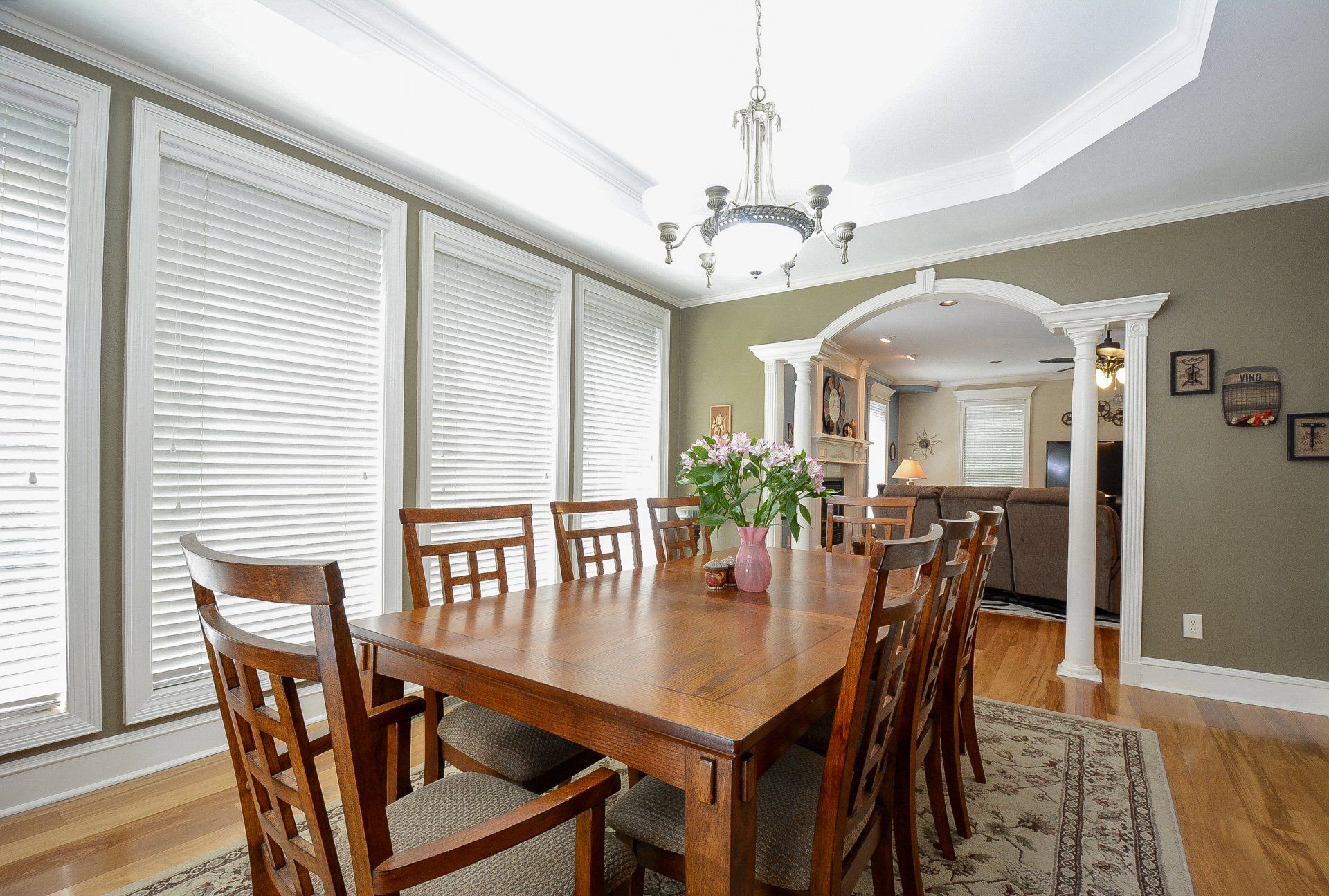 Dining room with wooden table and chairs, windows with blinds, and a view into another room.